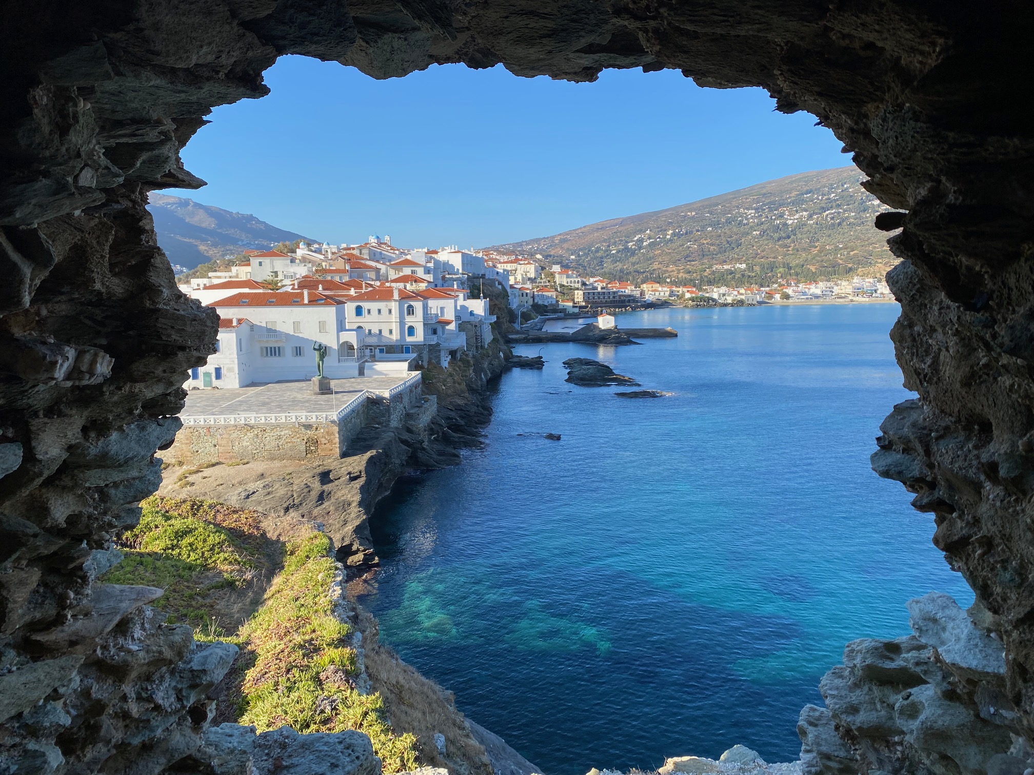 White buildings with red roofs in Chora seen through arch in remains of Venetian castle