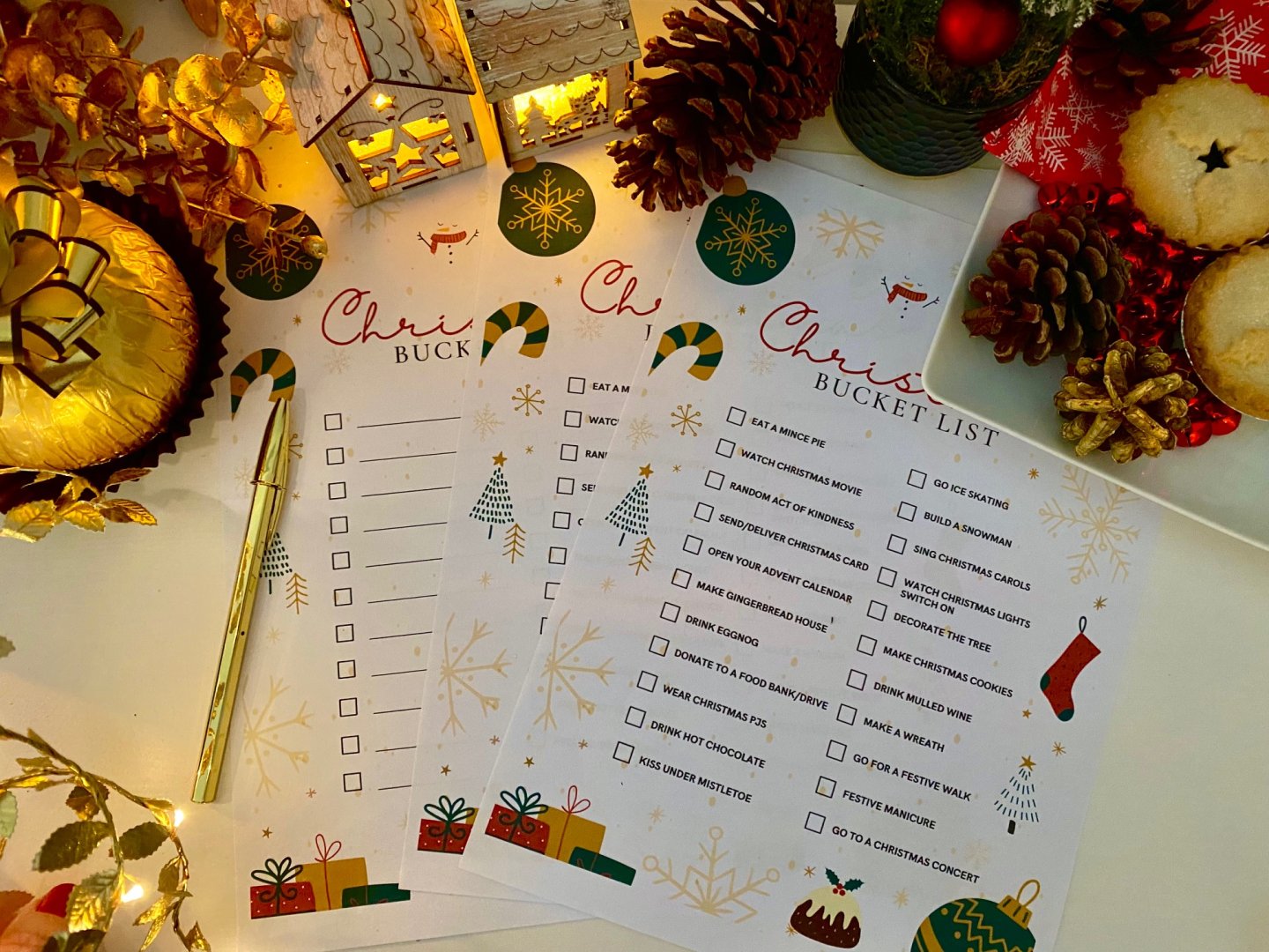 3 Christmas bucket list printable sheets on a table with gold pen, mince pies and other festive decorations