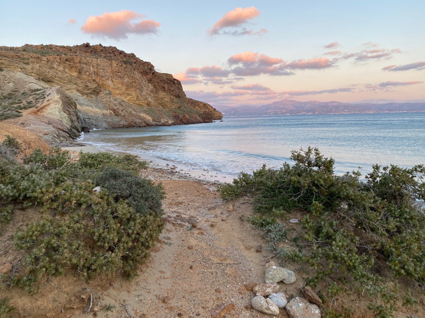 Sandy path leading to a beach with rock cliff at sunset