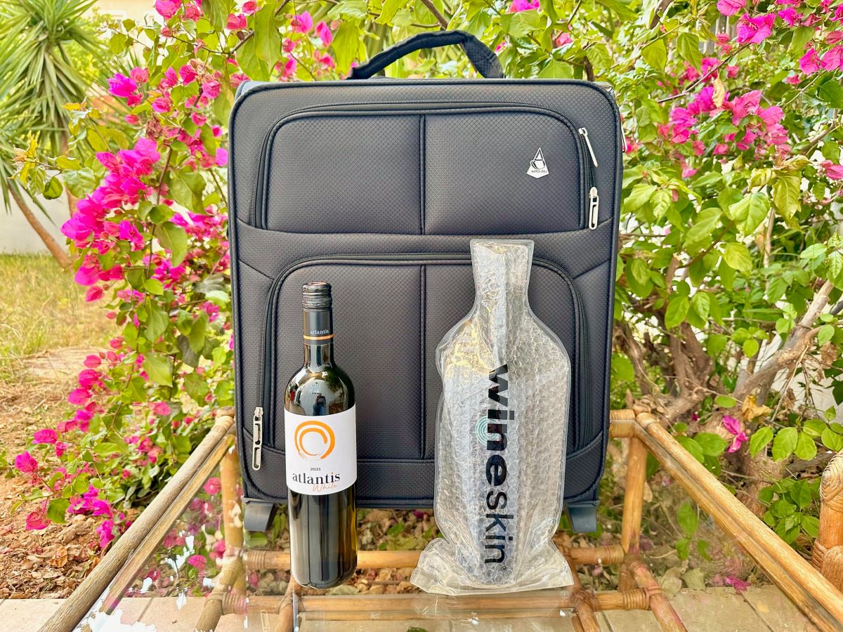 Black soft-sided suitcase with bottle of atlantis wine and bottle in a plastic wine skin