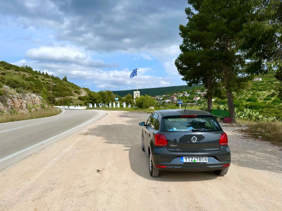 Grey VW Polo rental car parked on the side of the road by a Greek flag