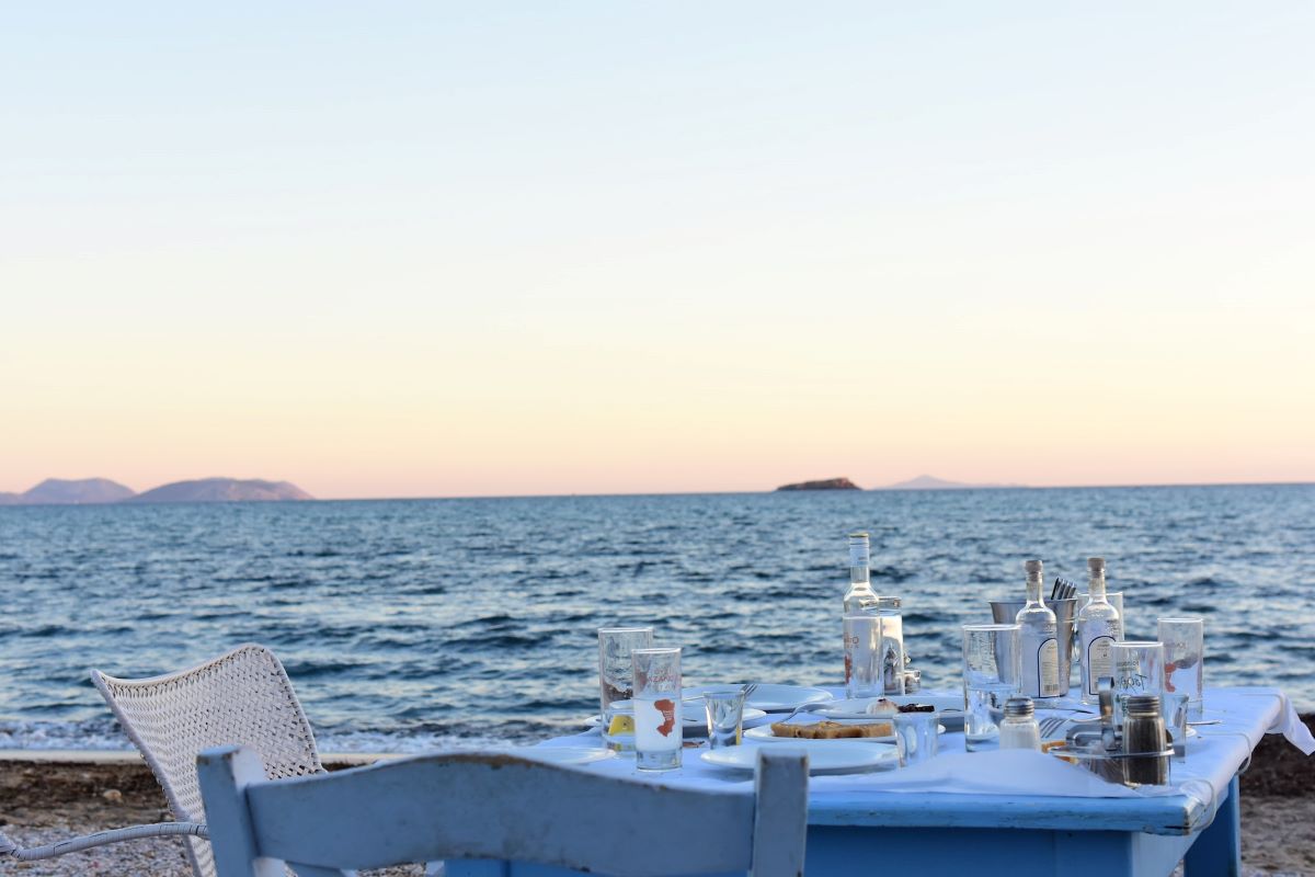 Blue wooden table at the beach at sunset with plates and ouzo bottles